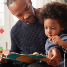 a dad reads to his child while they sit on his lap